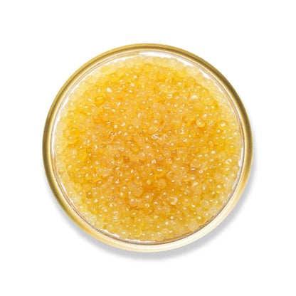 Close-up of a glass bowl filled with yellow caviar on a white background